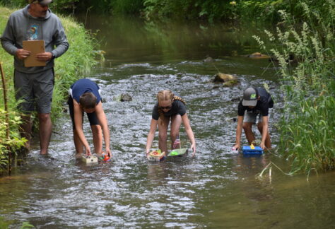 three children put play homemade boats into a stream