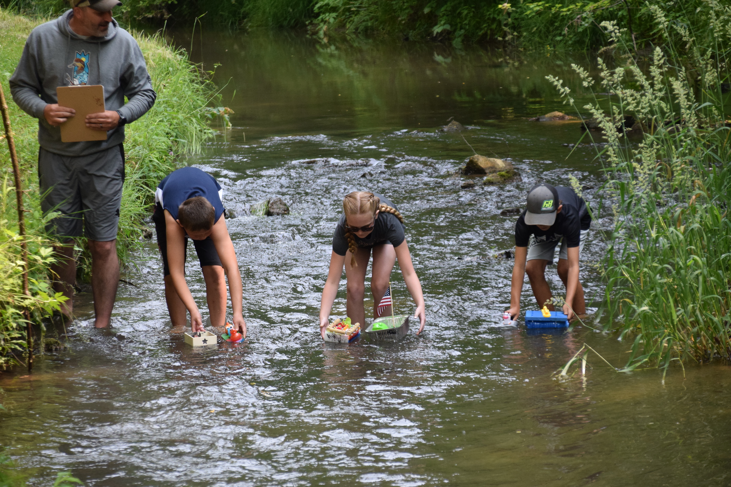 three children put play homemade boats into a stream