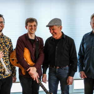 four musicians one holding a guitar and another a trumpet
