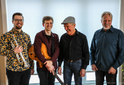 four musicians one holding a guitar and another a trumpet
