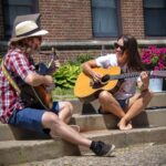 a man and woman sit on steps on a summer day playing guitar