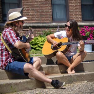 a man and woman sit on steps on a summer day playing guitar
