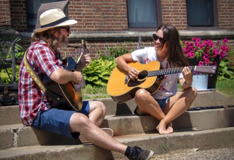 a man and woman sit on steps on a summer day playing guitar