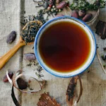 mug of lavender tea with spoon full of dried lavender sitting next to it on a wooden surface